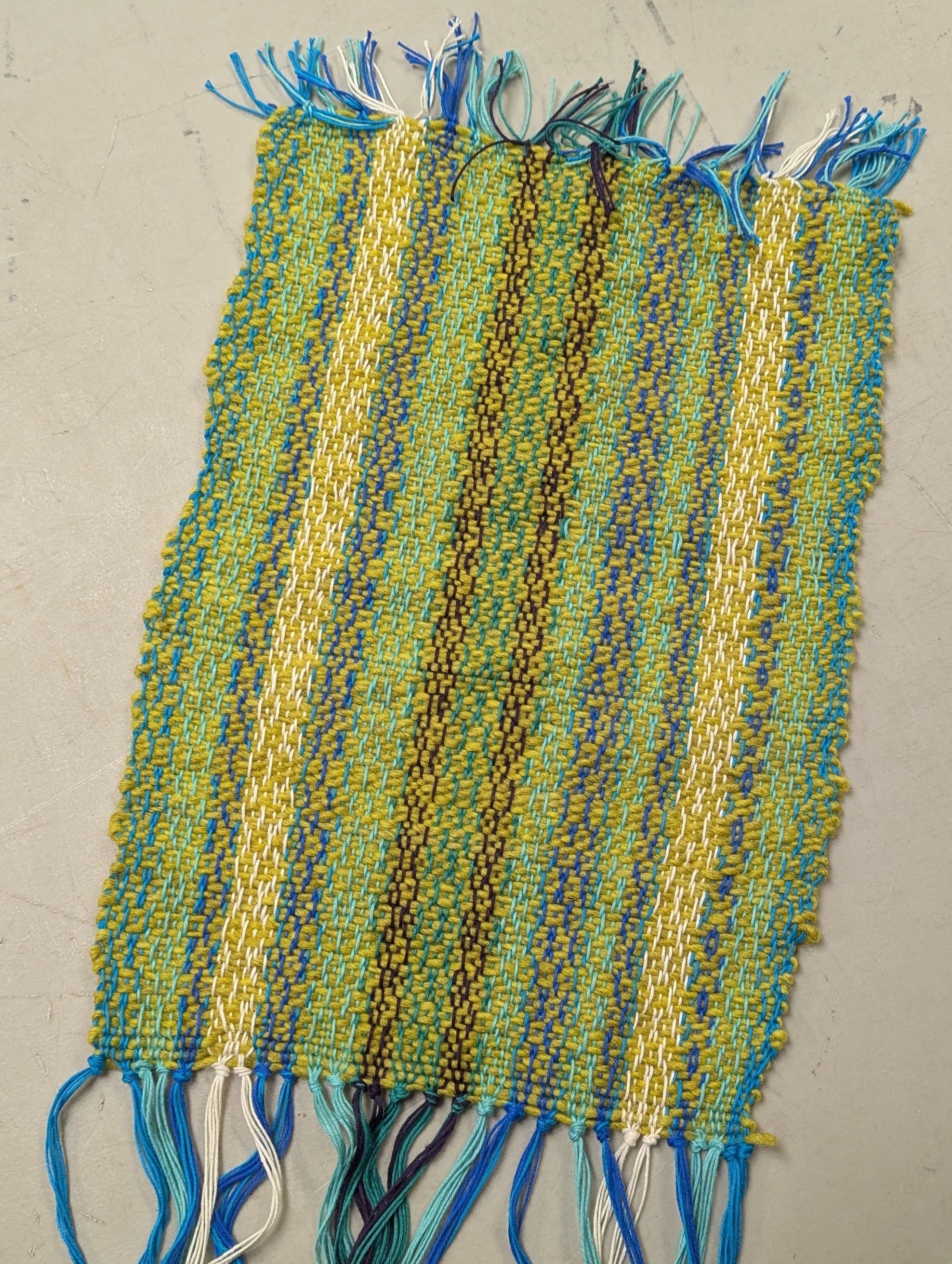 A small woven tapestry with stripes and hand-knotted, frayed ends.